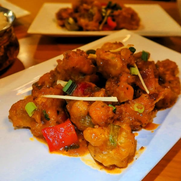 Close-up of Indian Manchurian chicken, garnished with red peppers and green onions, on a white plate.