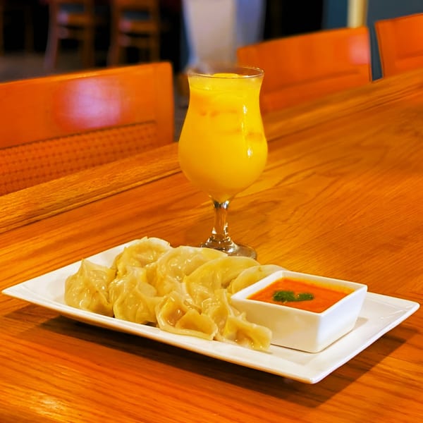 A plate of Indian momos with dipping sauce and a mango lassi on a wooden table.