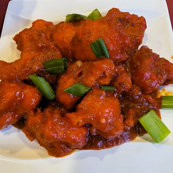 Taj Indian Restaurant's bright red chili chicken, garnished with fresh green onions on a white plate.
