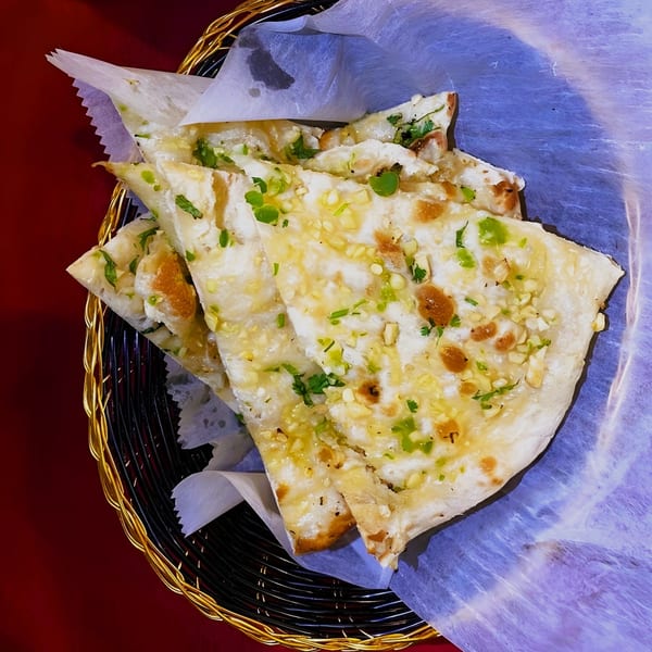 Golden basket filled with garlic naan bread, garnished with green herbs, from Taj Indian Restaurant.