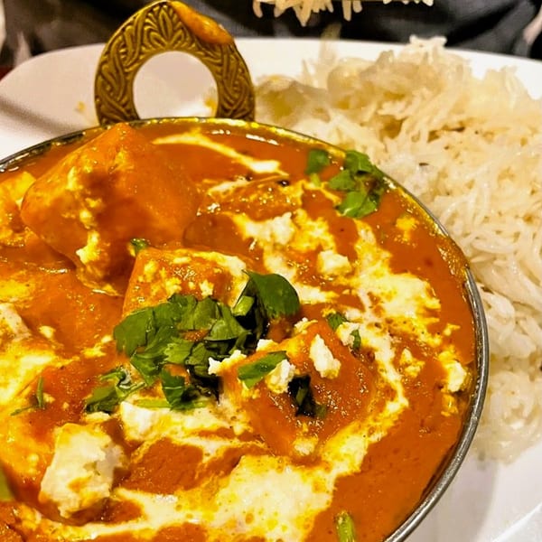 Taj Indian Restaurant's Paneer Butter Masala, a rich orange curry with paneer, cream, and cilantro, served with rice.